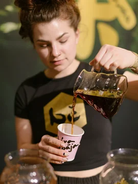 Baristka nalieva filtrovanú kávu do potlačeného papierového pohára